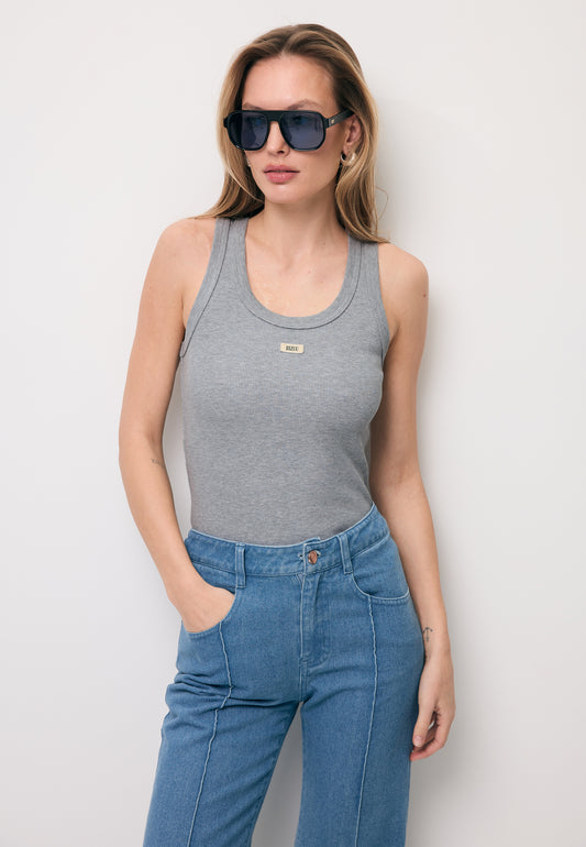Modelka z jedną ręką w kieszeni jeansów ubrana w szary top z prążkowanej dzianiny EJRIS.