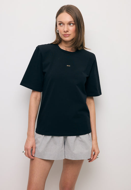 Modelka patrząca w bok ubrana w czarny T-shirt MELISA z poduszkami na ramionach.