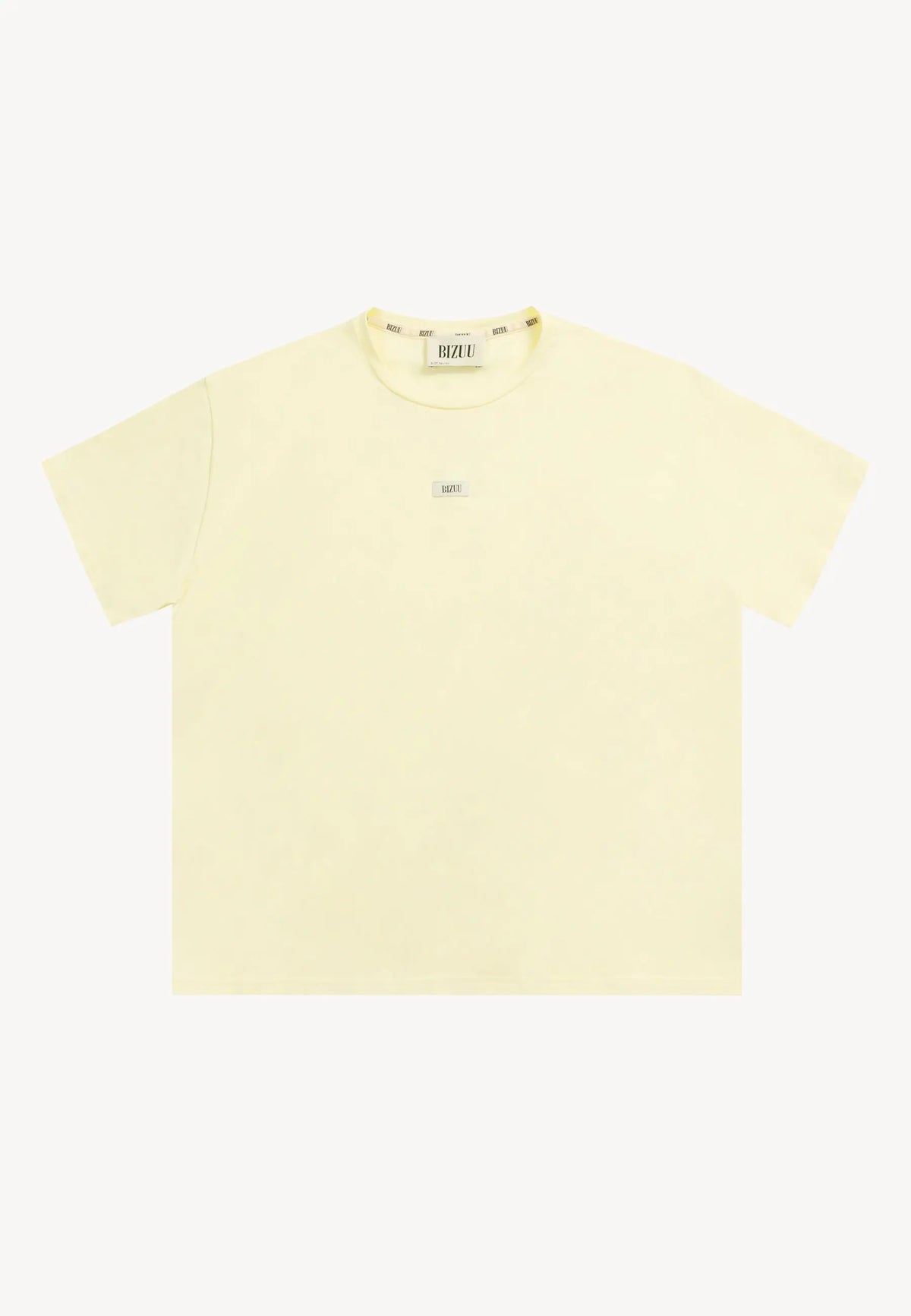 Modelka na białym tle z rękoma z tyłu w masełkowym T-shircie TISHALLE i jeansowych szortach MENORCA.