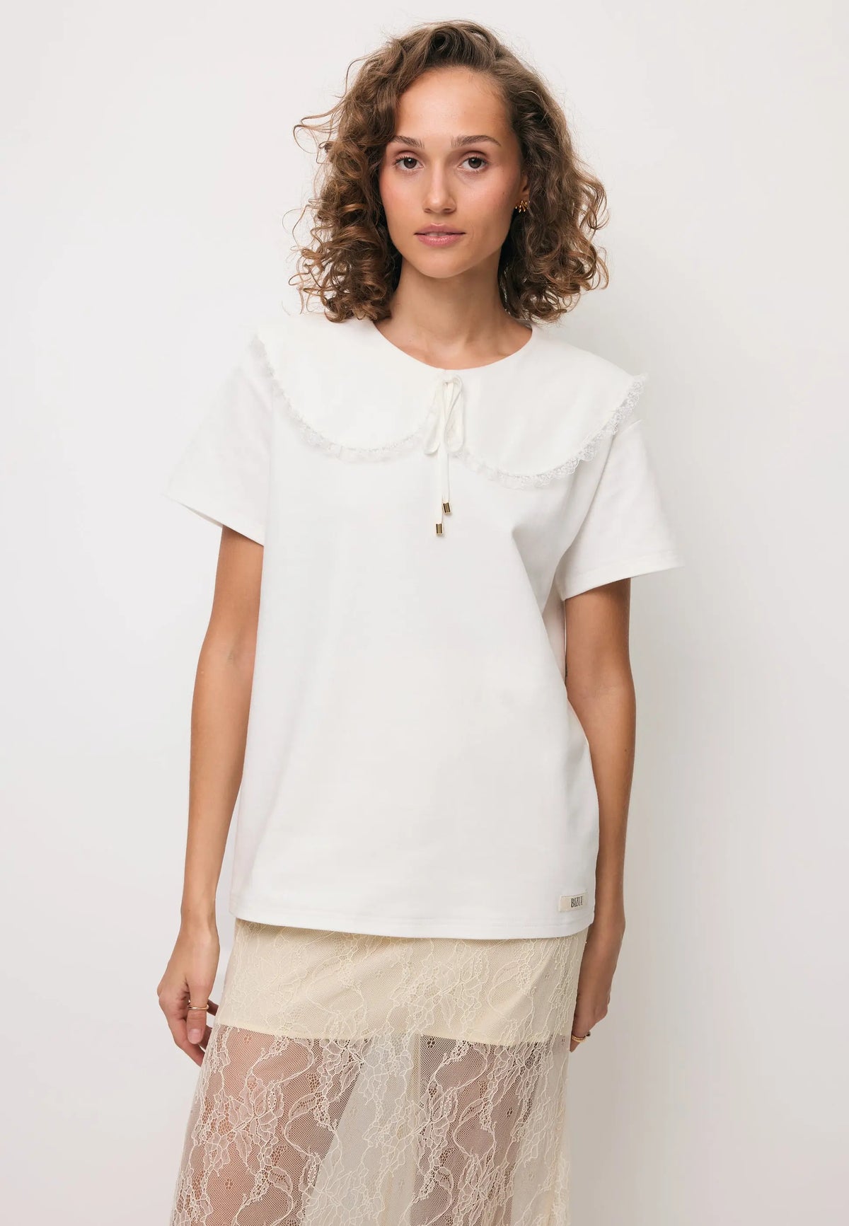 Zbliżenie na modelkę w kremowym T-shircie z ozdobnym kołnierzem CUTIE i kremowej spódniczce z koronki FLACE.