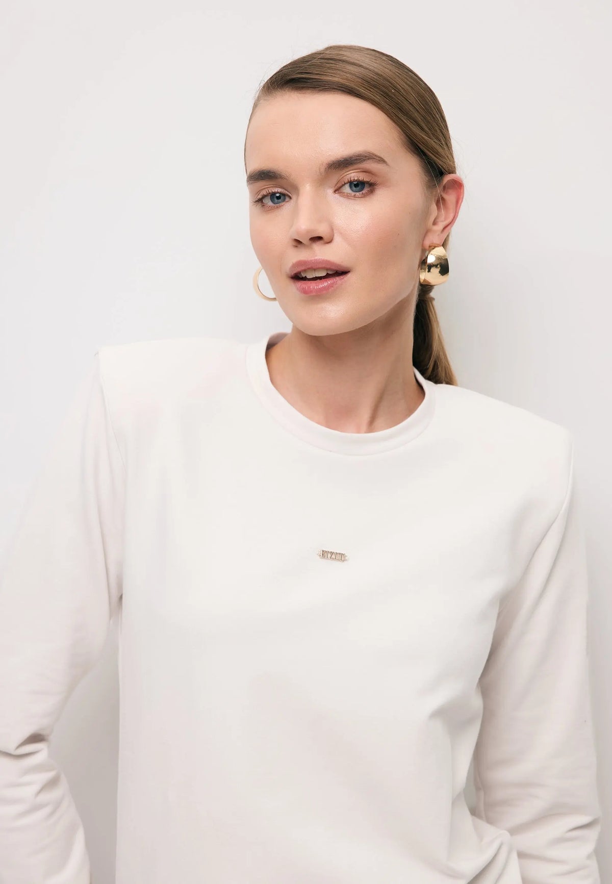 Zbliżenie na modelkę w kremowym longsleeve MELISSANDRA z poduszkami na ramionach.