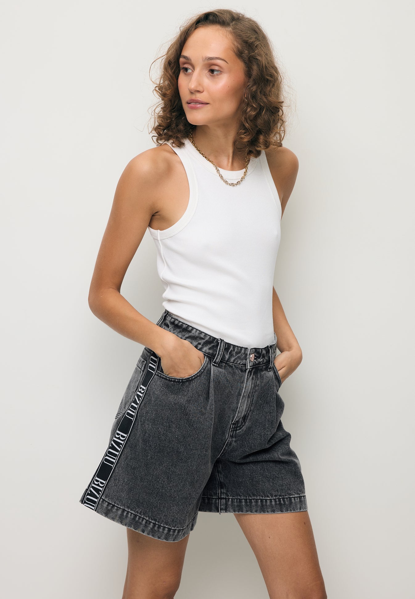 Modelka ubrana w czarne jeansowe shorty z logowaną taśmą z boku MIREYA.