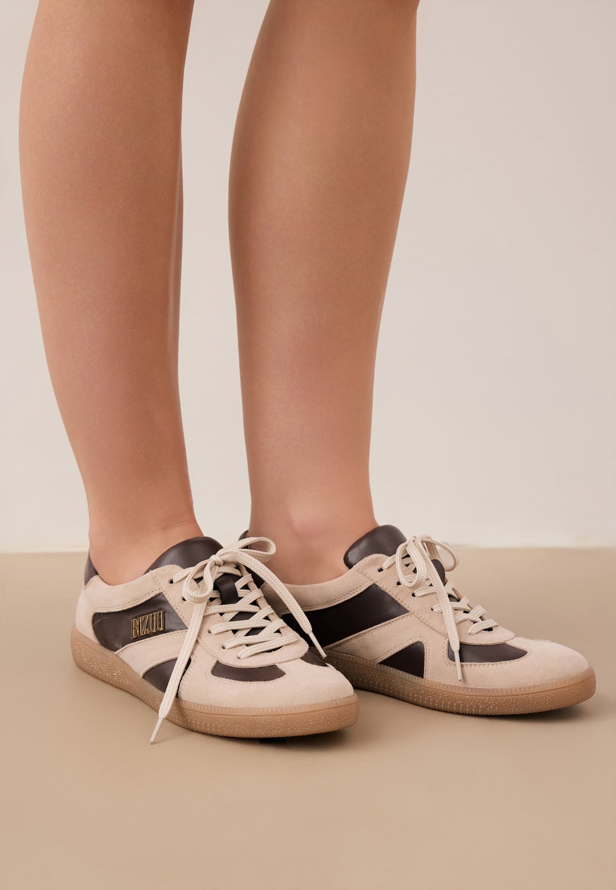 Zbliżenie na nogi modelki w beżowych sneakersach SODDY z brązowymi wstawkami.