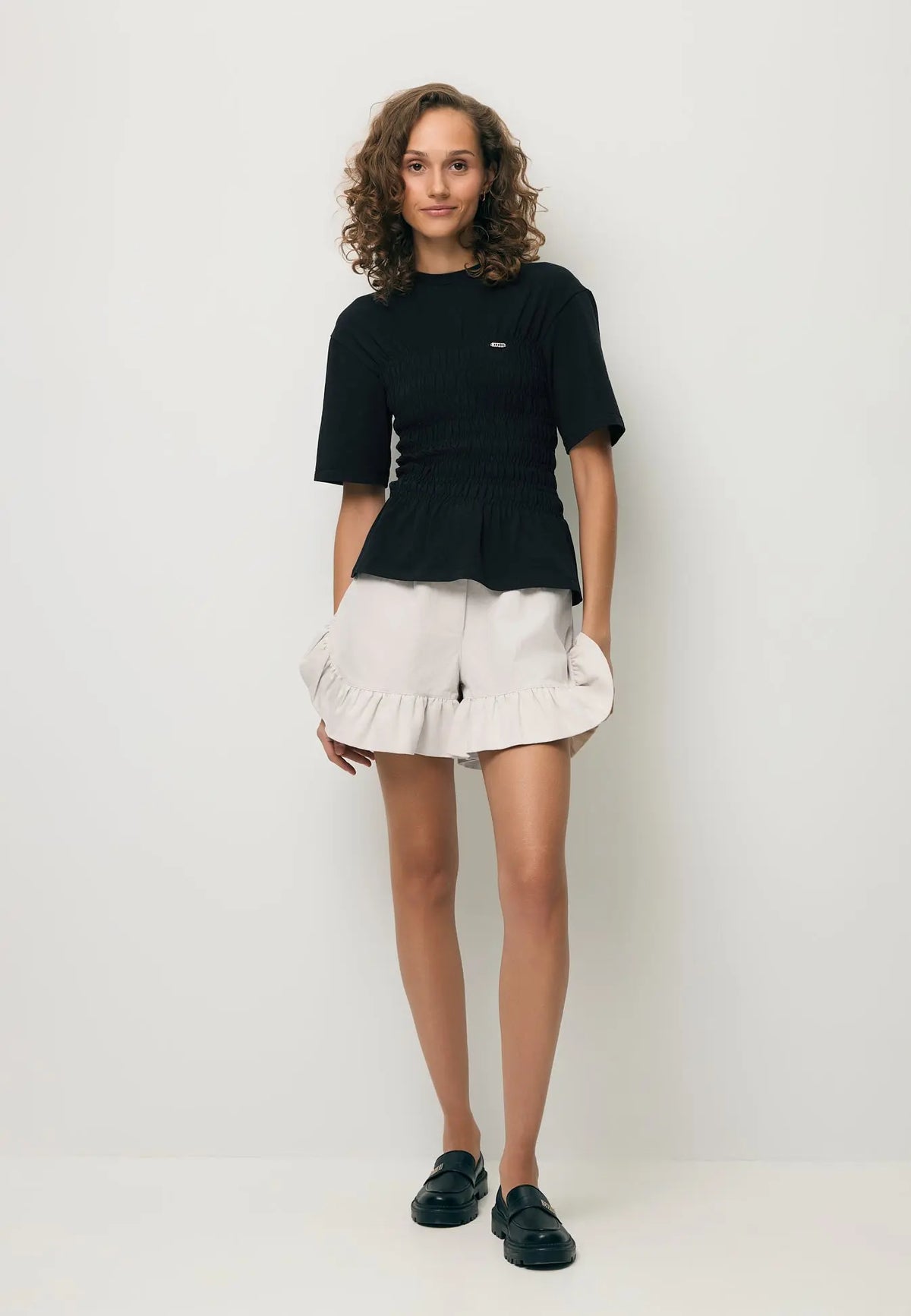 Modelka ubrana w czarny T-shirt SORIA oraz kremowe spodenki NEYO.