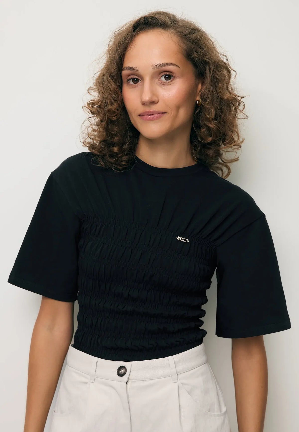 Zbliżenie na modelkę w czarnym T-shircie SORIA z metalowym logo.